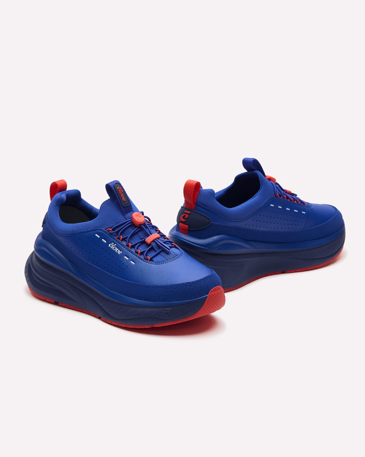 A pair of blue athletic sneakers with red accents, including the laces, pull tabs, and bottom tips, displayed on a clean off-white background.