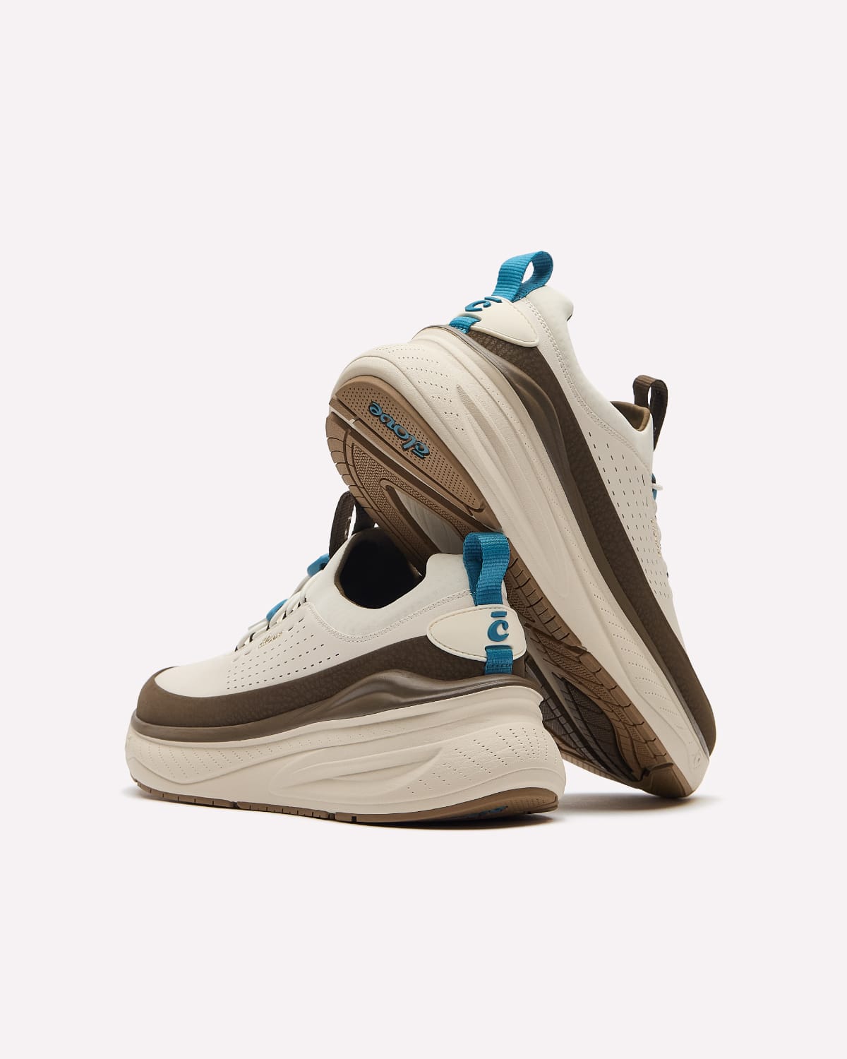 A pair of chunky platform sneakers in off-white, brown, and black, featuring bright blue pull tabs and laces, displayed on a clean white background.