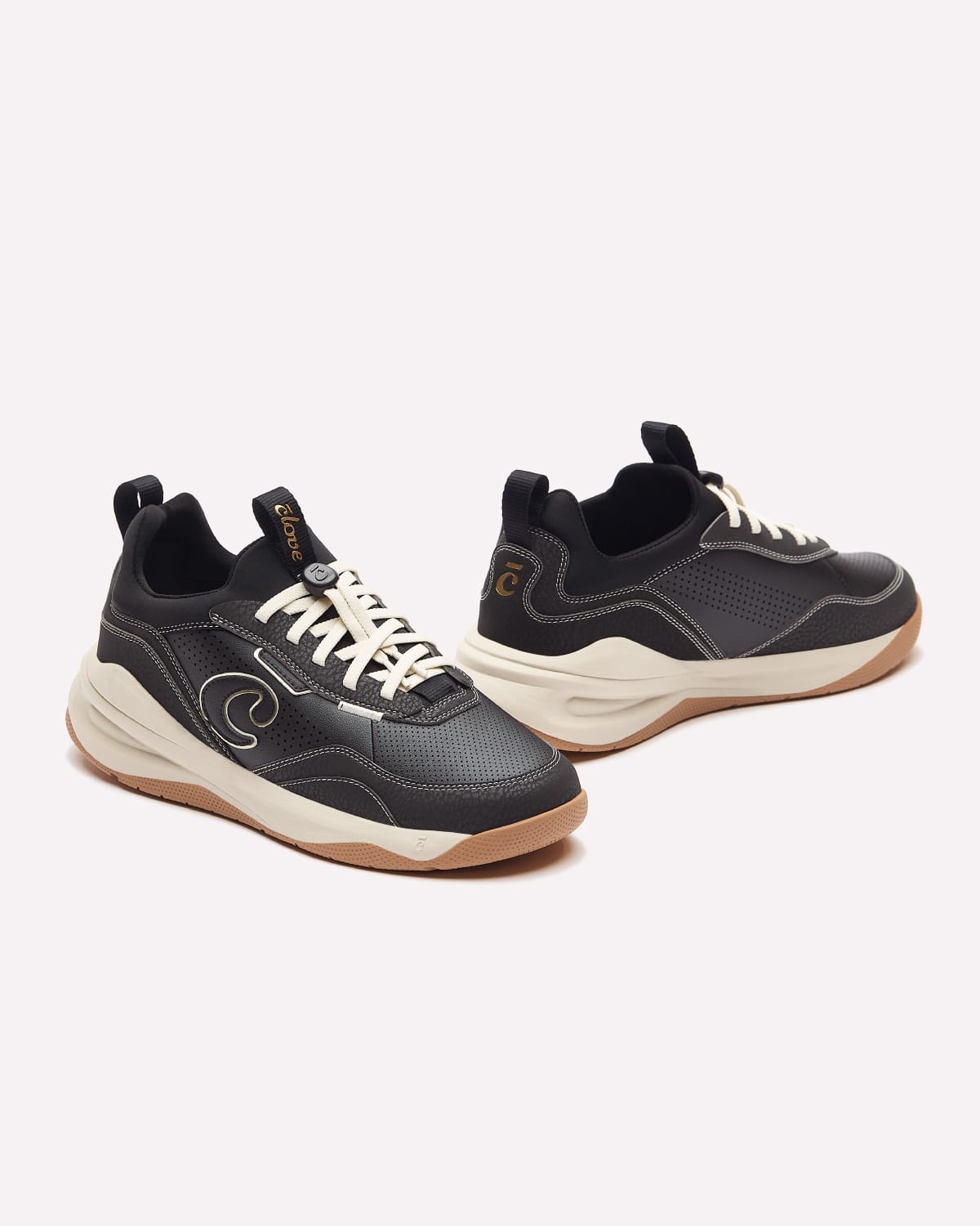 A pair of black and dark gray low-top sneakers with cream laces and a gum bottom, displayed on a light off-white background.
