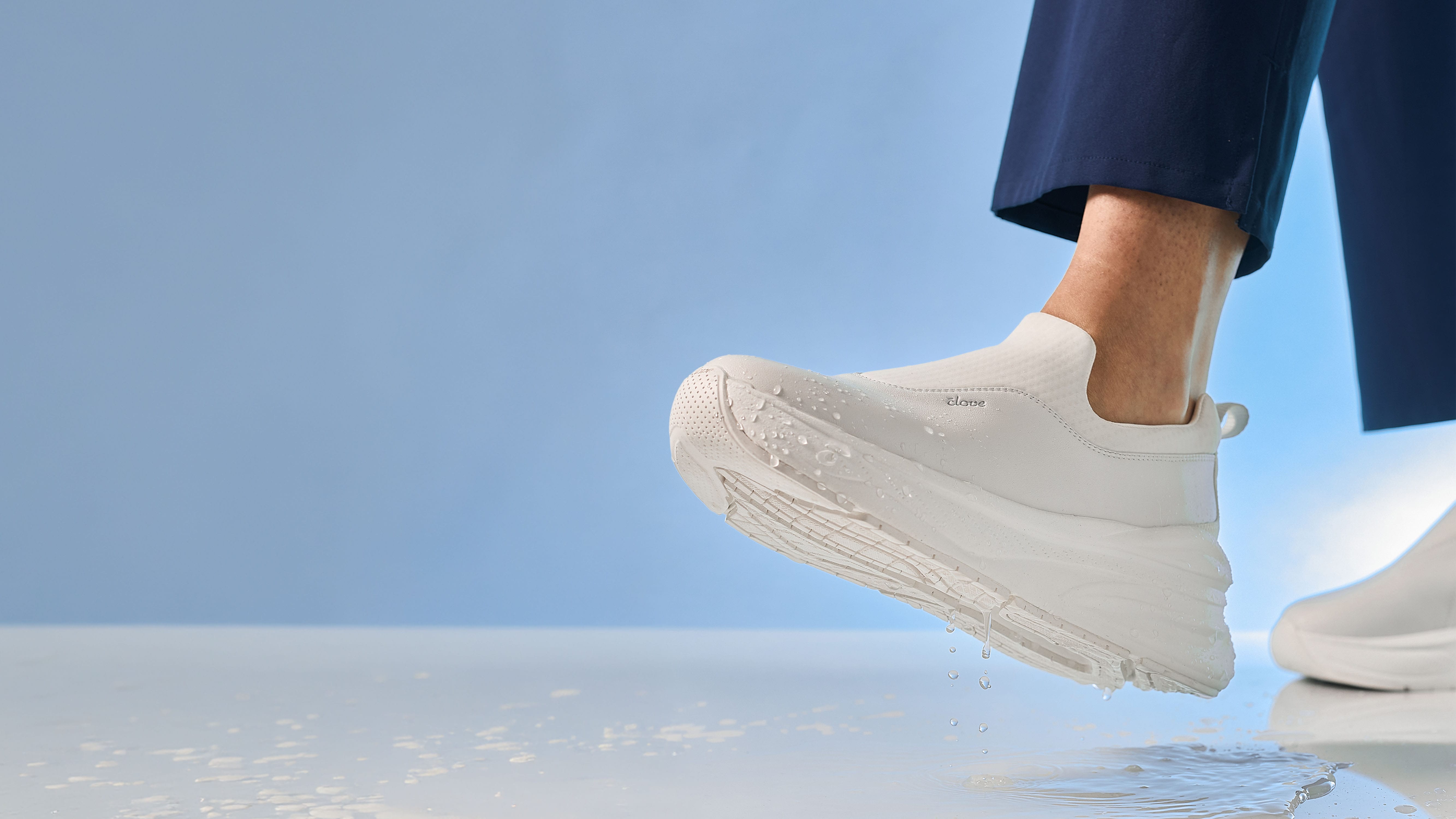 White sneakers worn by a person standing on a reflective surface with a blue background