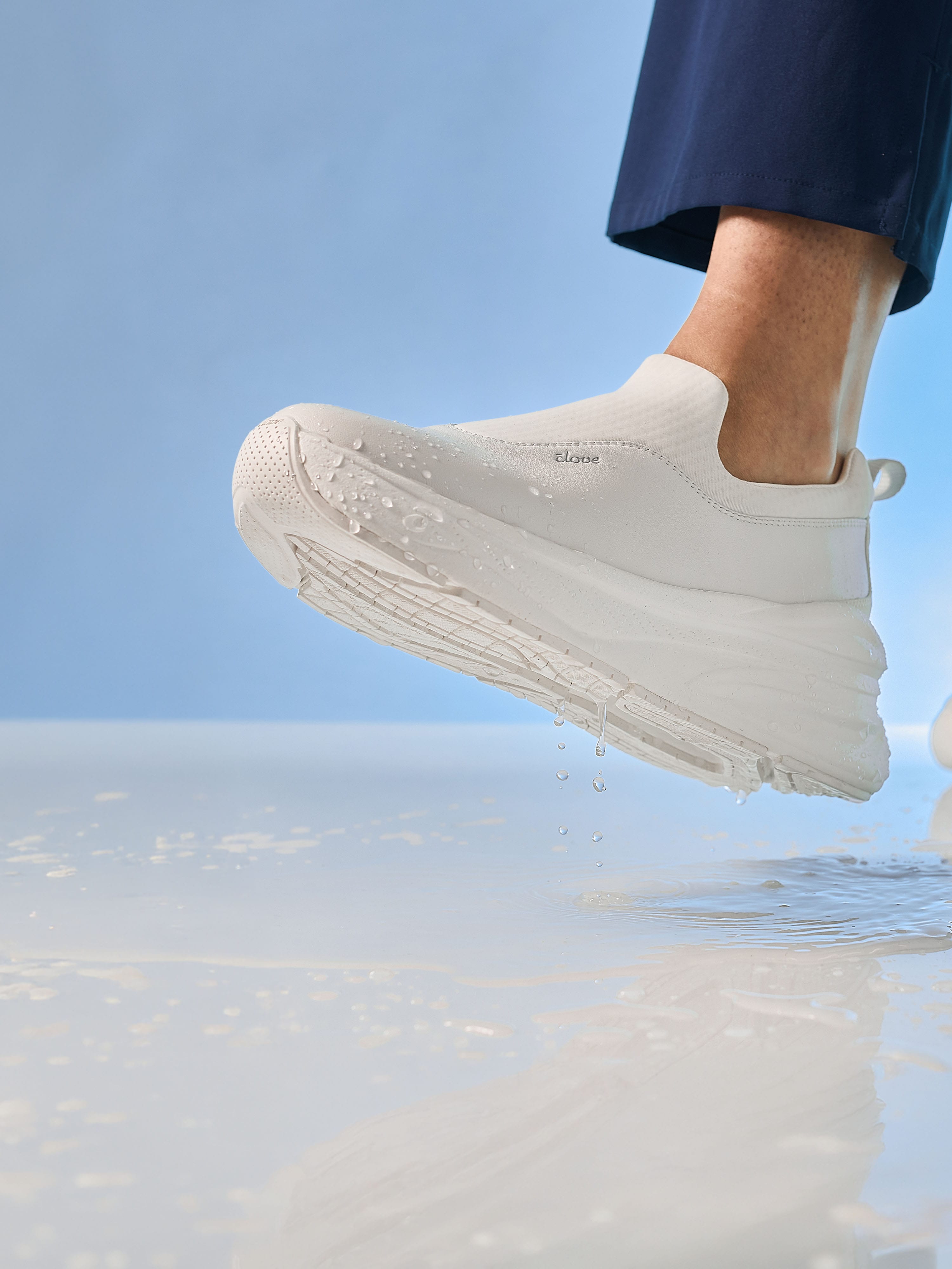 White sneaker with a brand logo on a clear water surface and blue sky background