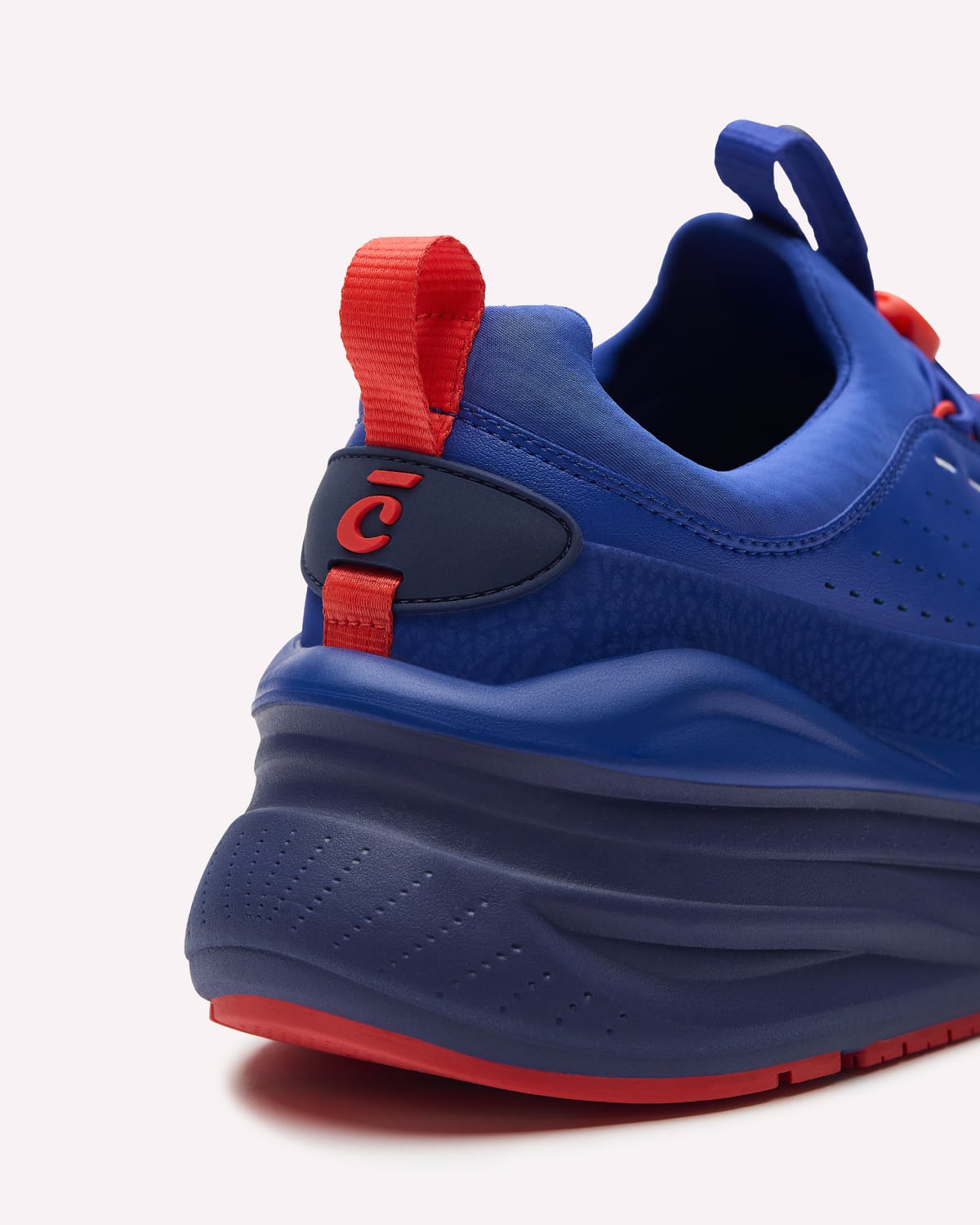 A blue sneaker with red accents, including the bottoms, laces, and pull tabs, displayed on a clean off-white background.