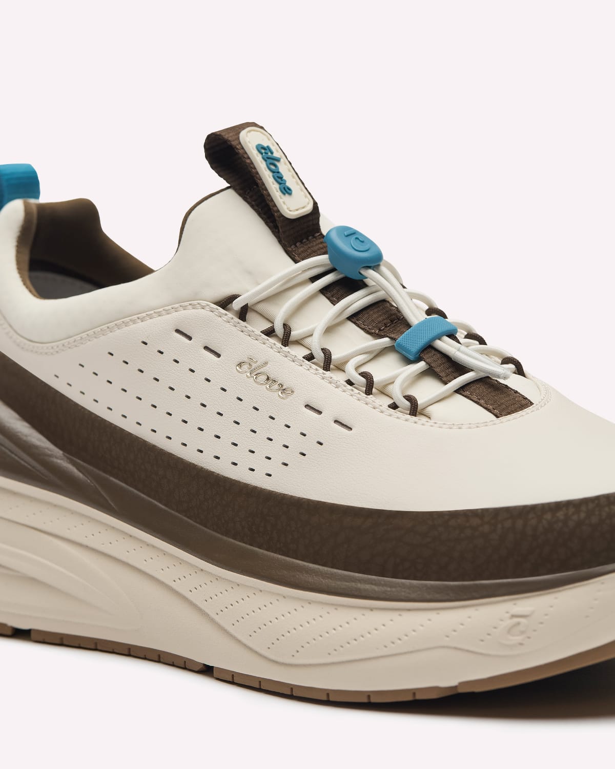 A close-up of a shoe in off-white and brown with laces and pull tabs, set against a clean off-white background.