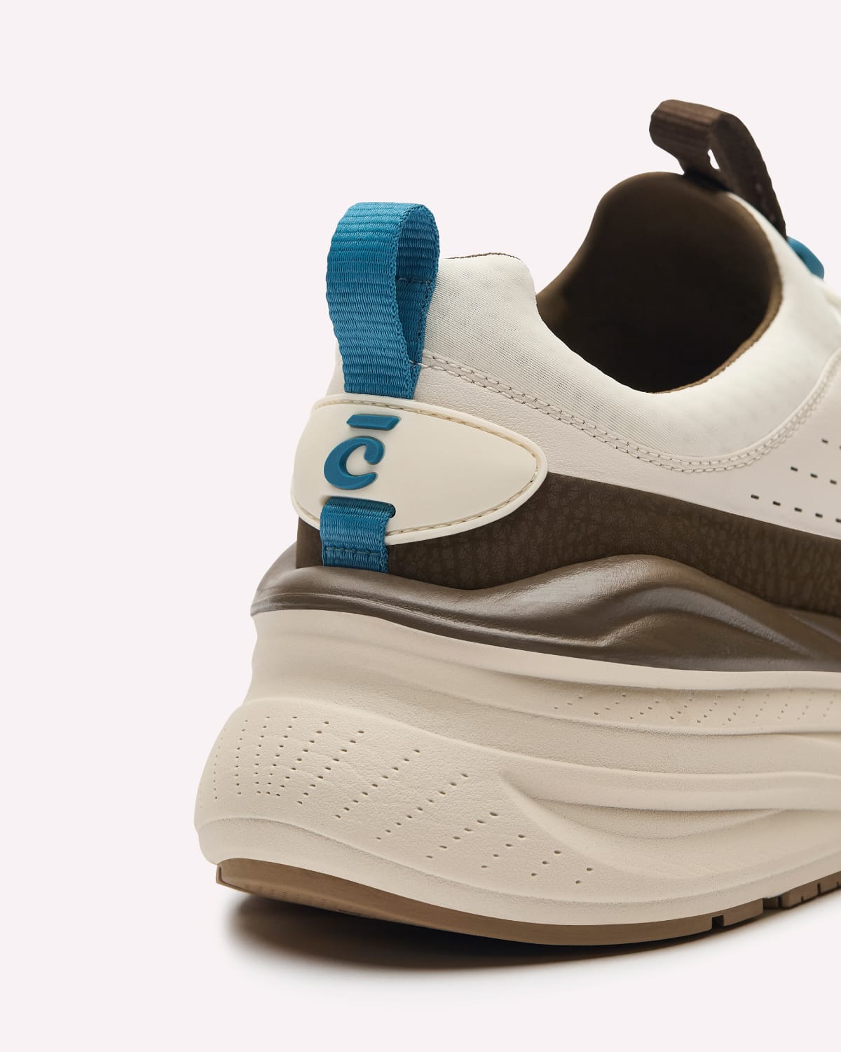 A close-up shot of the heel and side of a chunky platform sneaker. The shoe features a white upper, a dark brown mid-section, a thick cream-colored platform bottom, and a bright blue pull tab with a blue 'C' logo.