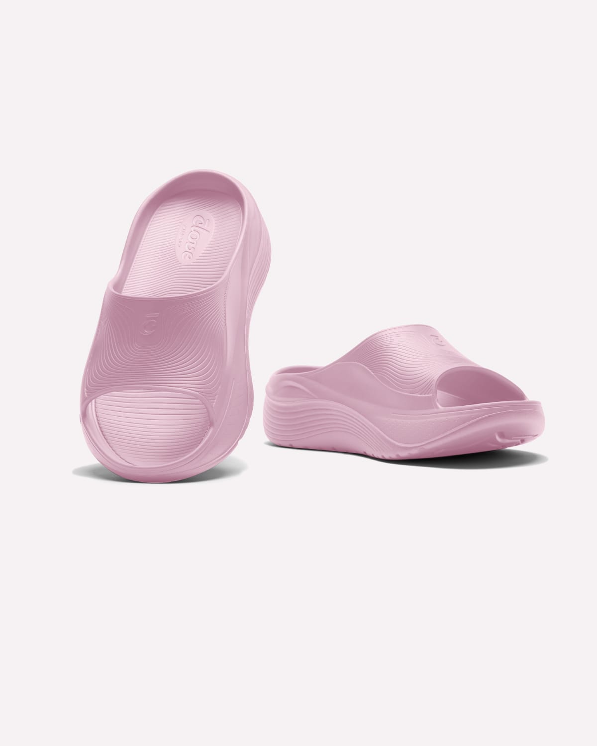 A pair of light pink molded foam slide sandals shown on a clean off-white background, with one sandal standing upright and the other lying on its side.