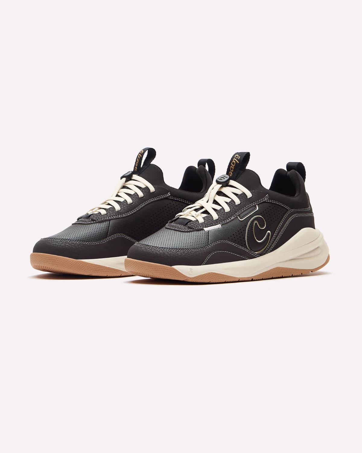 A pair of black and dark gray athletic sneakers with cream laces, a cream mid-section, and gum brown bottom, shown against a light gray background.