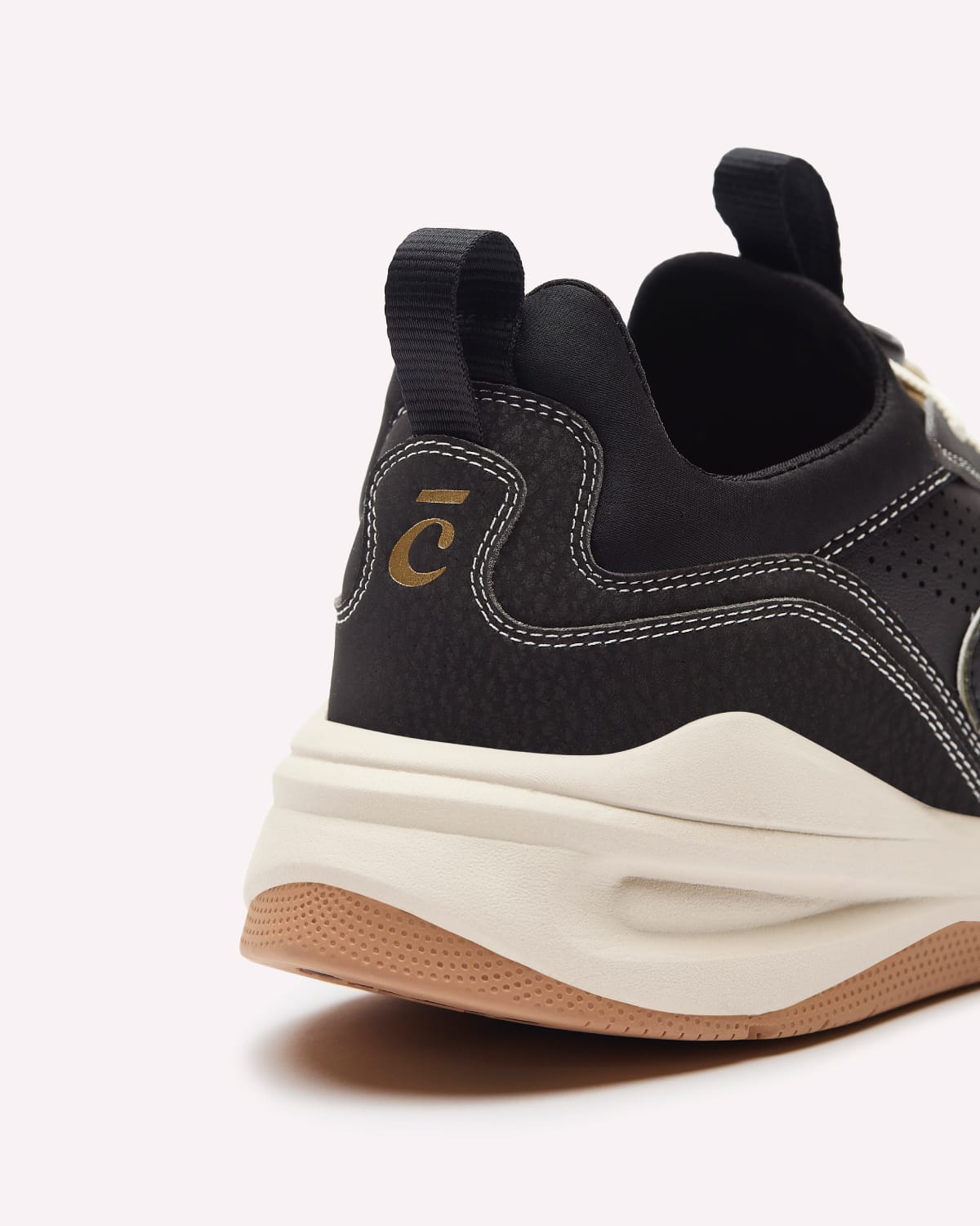 Close-up rear three-quarter view of a black athletic sneaker with a chunky off-white mid-section and a tan bottom, featuring a gold stylized 'C' logo on the heel.
