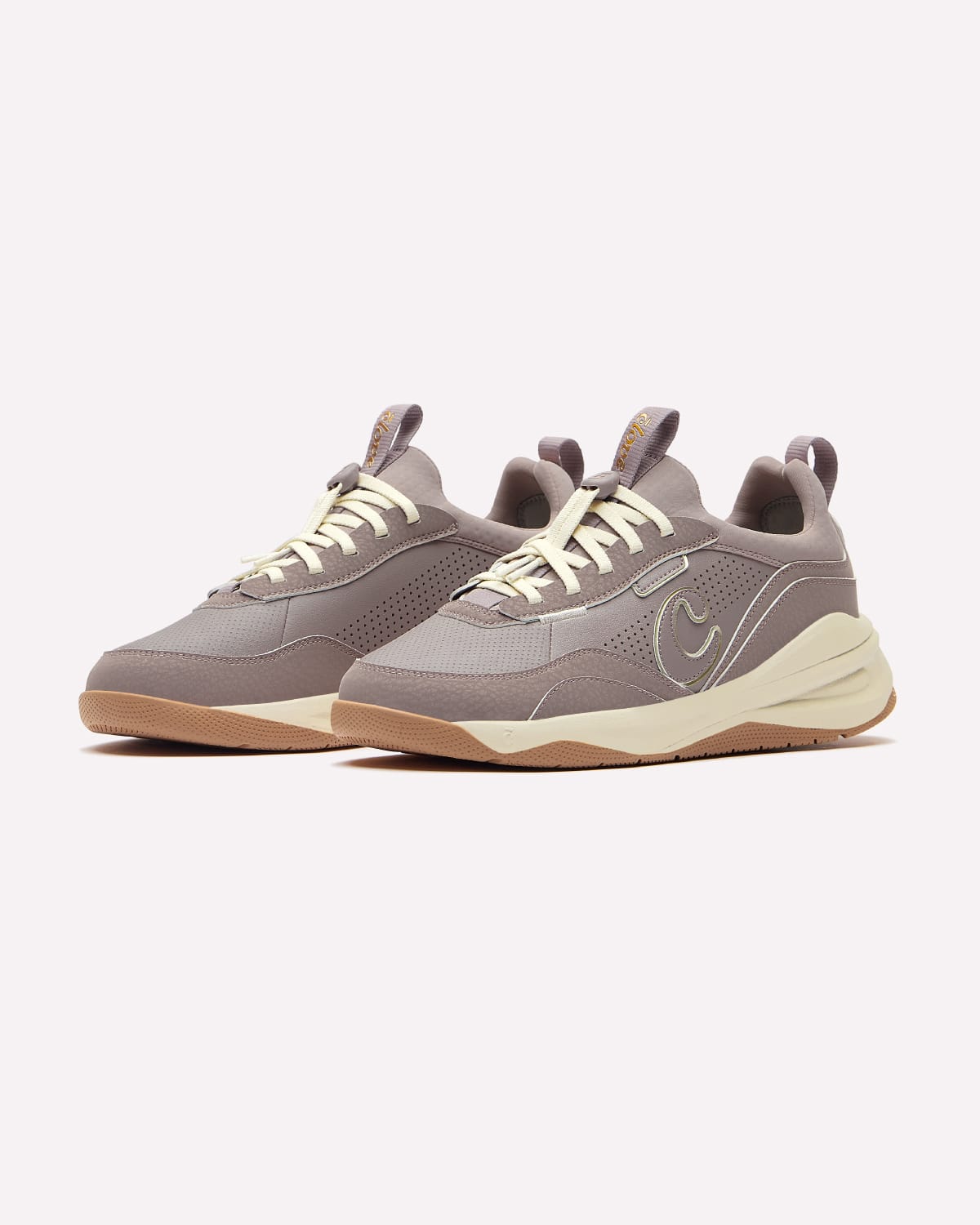 A pair of sneakers in a muted taupe-gray colorway, featuring cream-colored laces and a chunky cream mid-section with a gum botom, set against a plain off-white background.