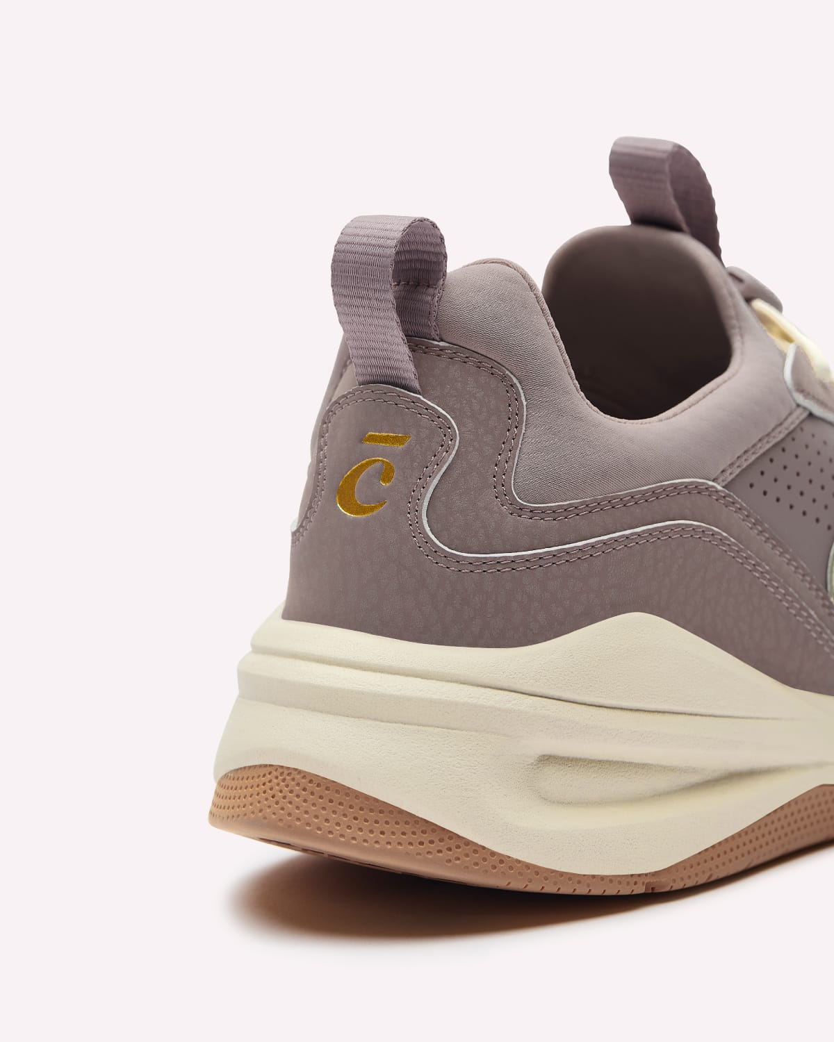 A close-up rear three-quarter view of a low-top sneaker in taupe and cream, featuring a gold stylized 'C' logo on the heel, a thick cream mid-section, and a gum bottom.