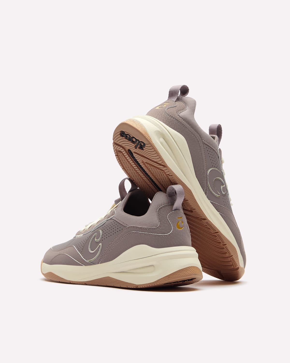 A pair of sneakers in taupe gray and cream, with one shoe standing upright to show the bottom and the other lying flat to show the side profile, set against a plain light gray background.