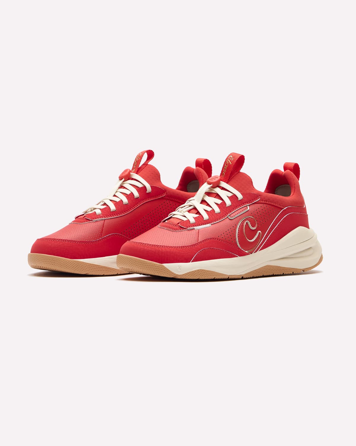 A pair of red low-top sneakers with white laces, a cream mid-section, and a gum bottom, displayed against a light gray background.