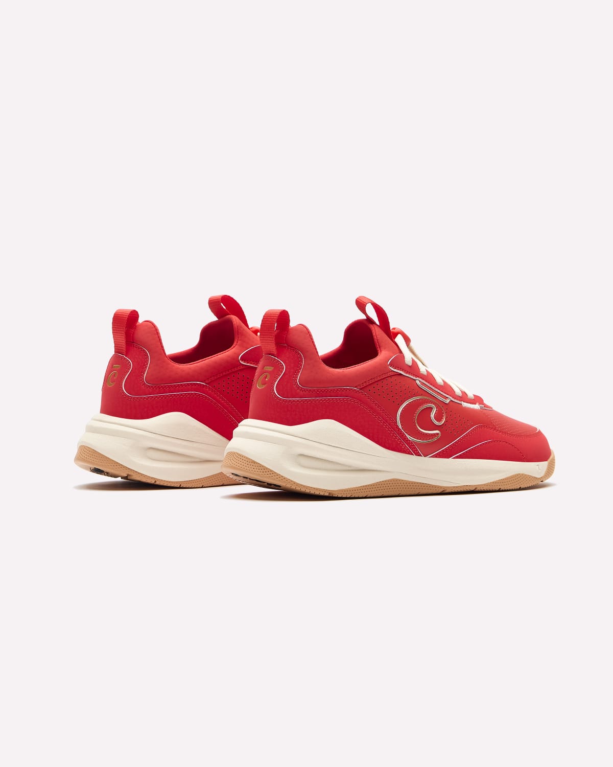 A pair of red athletic sneakers with cream-colored mid-section and gum bottoms, displayed from a three-quarters angle on a light gray background.