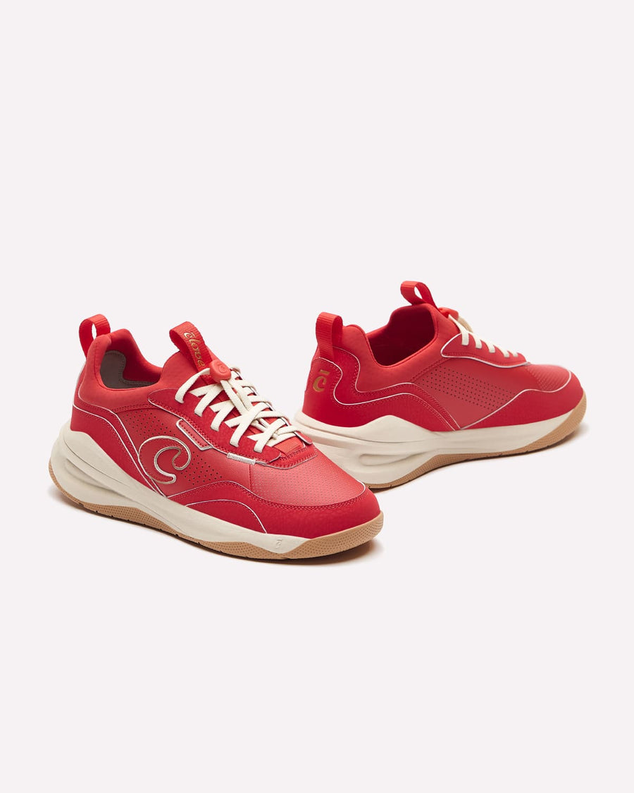 A pair of red low-top sneakers with cream laces and a thick cream and gum bottom, displayed on a clean off-white background.